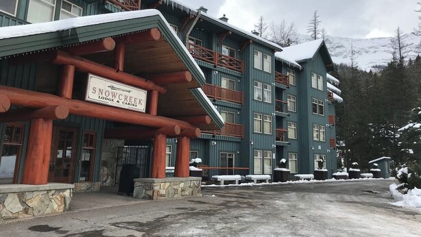 Un chalet dont l’enseigne indique « Snow Creek Lodge & Cabins », avec une façade en bois et des fondations en pierre.