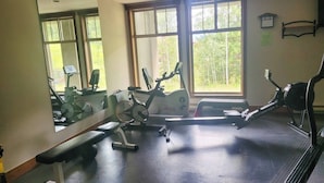 Une salle de sport équipée de matériel d’exercice, d’un banc et de grandes fenêtres.