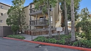 Un edificio de apartamentos de varios pisos con balcones, rodeado de árboles y una acera roja.