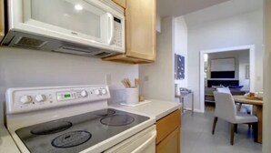 Cocina con microondas, estufa y armarios de madera. Hay un comedor con mesa y sillas.