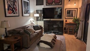 Una sala de estar con sofá, televisión, chimenea y obras de arte enmarcadas en la pared.