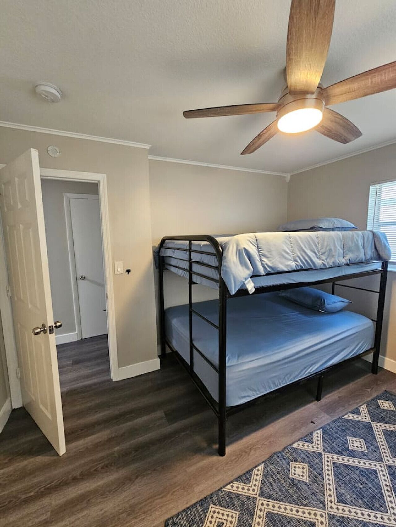 A bunk bed room with a ceiling fan, a patterned rug, and a door leading to another room.