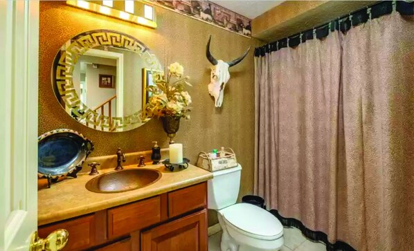 A bathroom with a sink, mirror, toilet, and a decorative skull on the wall.