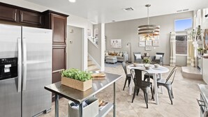 Una cocina moderna con un refrigerador de acero inoxidable, un comedor con una mesa redonda y sillas, y una escalera que lleva a una sala de estar con un sofá y objetos decorativos.