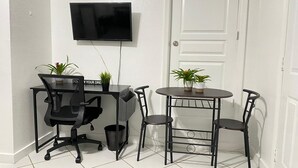 Ett litet kontorsutrymme med ett skrivbord, en stol och ett runt bord med två stolar. En tv är monterad på väggen, och det står två krukväxter på skrivbordet och bordet.