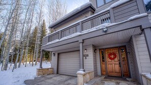 A two-story house with a stone entrance, a garage, and a wooden front door with a wreath. - Private 5 Bedroom East Vail Getaway by Gorecreek Rentals (Vail)