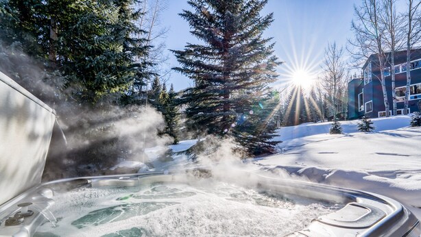 A hot tub surrounded by snow-covered ground and trees, with a clear sky and sun shining. - Private 5 Bedroom East Vail Getaway by Gorecreek Rentals (Vail)