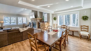 A spacious living area with a wooden dining table, comfortable seating, a fireplace, and large windows offering a view of trees. - Private 5 Bedroom East Vail Getaway by Gorecreek Rentals (Vail)