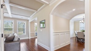A spacious living room with hardwood flooring, a grey sofa, and a dining area with a chandelier. - Masters Golf Rental, Overlooks Course (Evans)