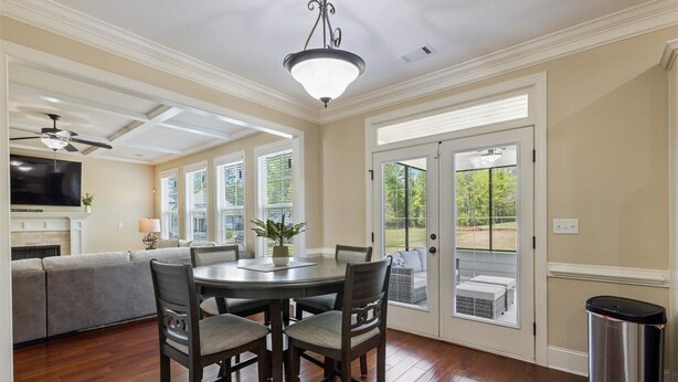 A dining area with a round table and four chairs, a ceiling fan, and a television in the background. - Masters Golf Rental, Overlooks Course (Evans)