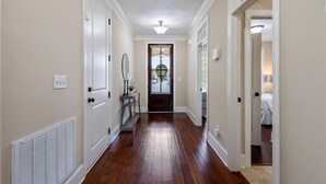 A hallway with wooden flooring, white walls, and a door leading to a bedroom. - Masters Golf Rental, Overlooks Course (Evans)