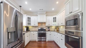 A modern kitchen with white cabinetry, stainless steel appliances, and a wooden floor. - Masters Golf Rental, Overlooks Course (Evans)