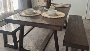 A dining area with a wooden table set for four, surrounded by a carpeted floor and a staircase.
