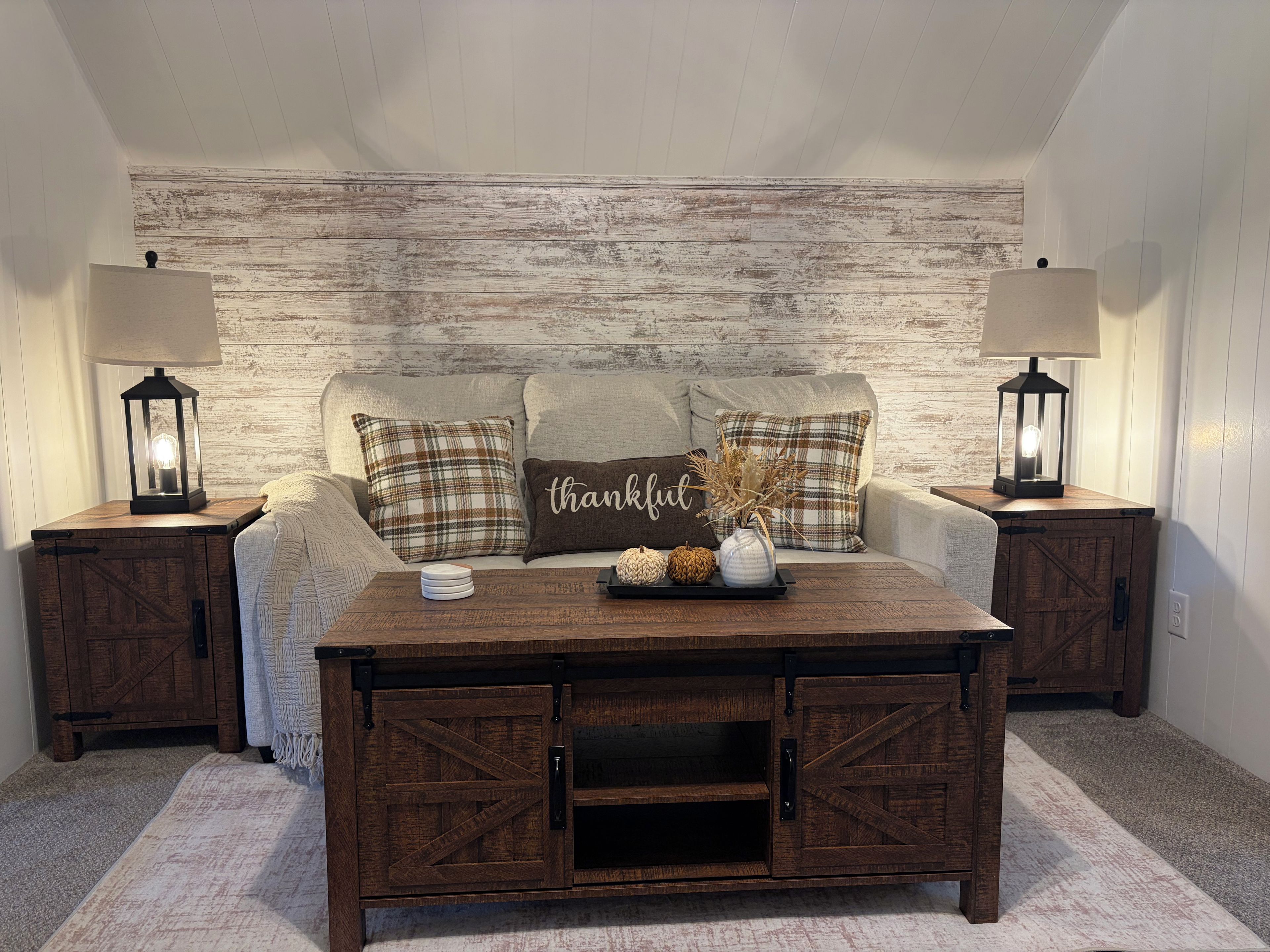 A cozy room with a sofa, two nightstands, a wooden coffee table, and a rustic wall.