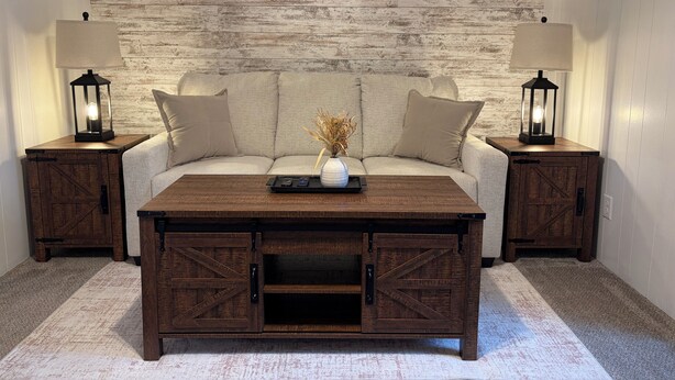A room with a sofa, two nightstands with lamps, a coffee table, and a rustic wall.