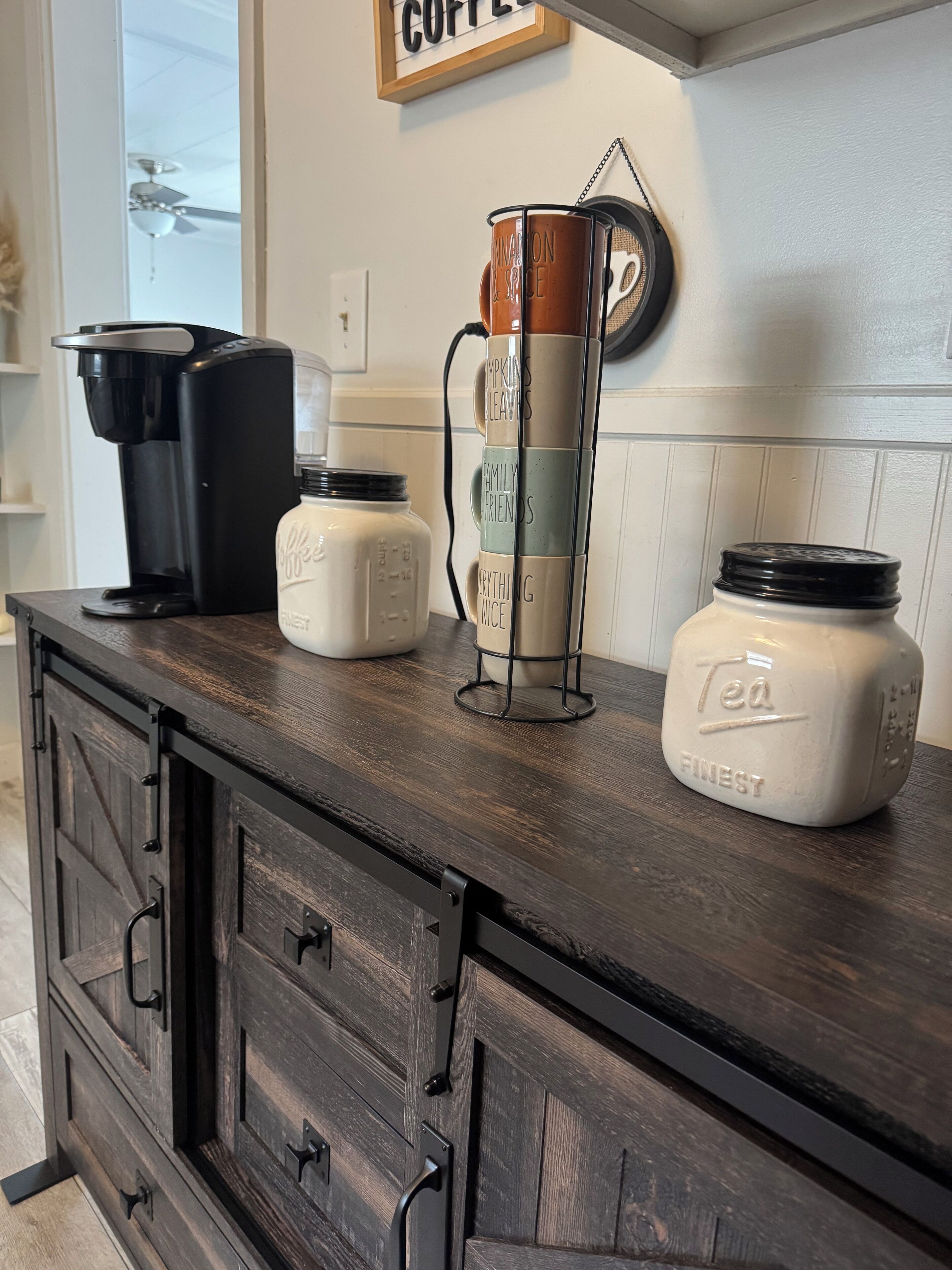 A kitchen counter with a coffee maker, a mug rack, and two jars labeled "Tea Finest".