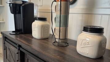A kitchen counter with a coffee maker, a mug rack, and two jars labeled "Tea Finest".
