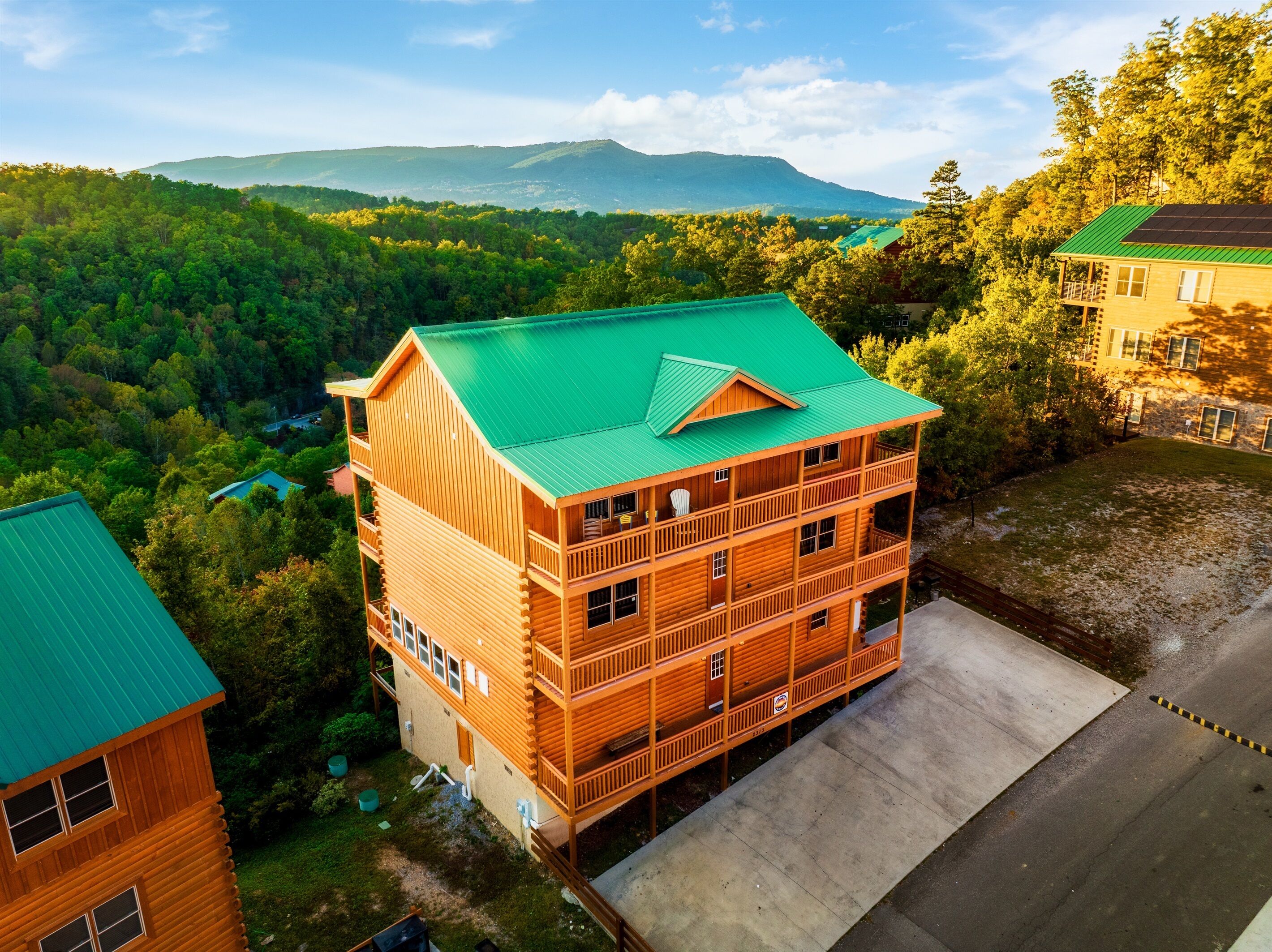 Une cabane en rondins à plusieurs étages, dotée d’un toit végétalisé, entourée d’une forêt dense et avec des montagnes en arrière-plan.