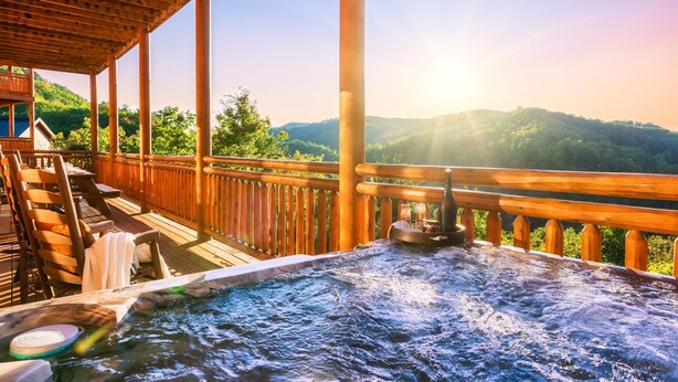 Une terrasse en bois avec un jacuzzi, des chaises en bois et une vue sur un paysage montagneux.