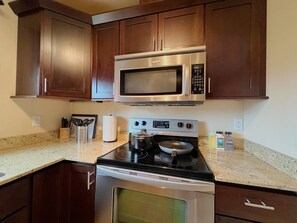 A kitchen with dark wooden cabinets, a stainless steel microwave, a stove, and a granite countertop.