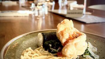 A plate of food with a piece of fish, noodles, and greens on a ceramic plate.