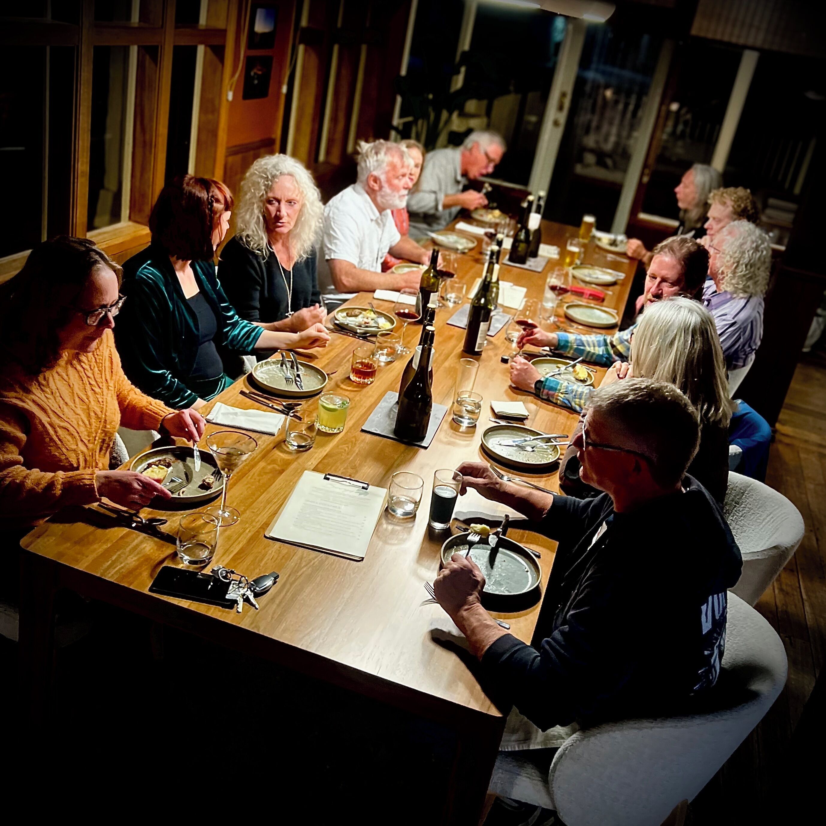 A group of people seated around a long wooden table in a dimly lit room.