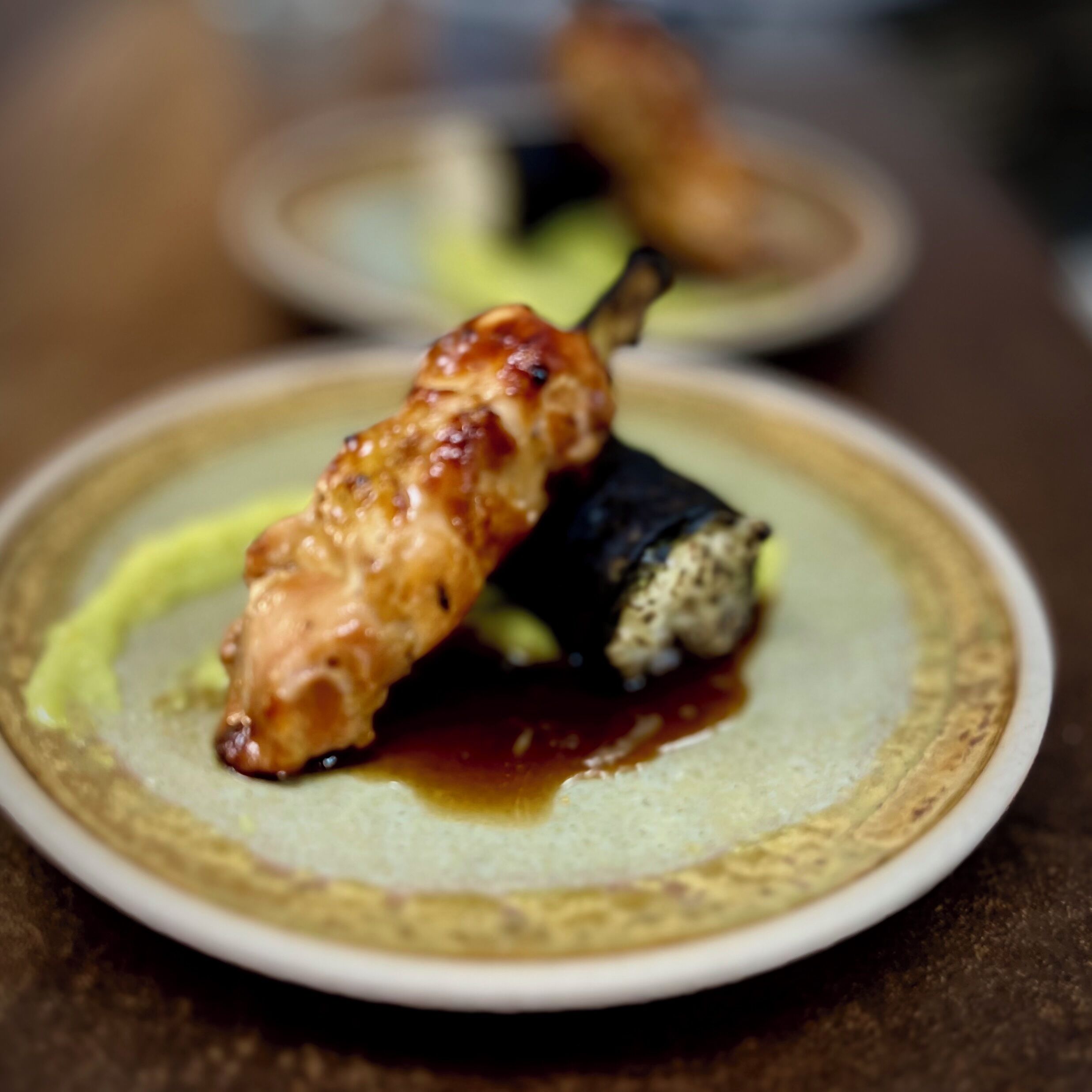 A plate with a skewered food item and a dark vegetable, possibly a dessert or appetizer, on a textured plate.