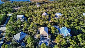 An aerial view of a coastal property with multiple buildings surrounded by dense forest, a clear view of the ocean, and a swimming pool area. - Top' Sea Turvy - Private Pool, 5 Minutes To Beach, Tennis & Pickleball Court! (St. George Island)
