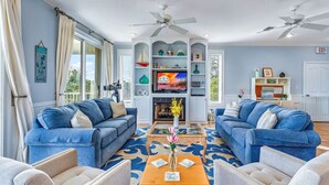 A living room with two blue sofas, a wooden coffee table with a vase, and a fireplace. - Top' Sea Turvy - Private Pool, 5 Minutes To Beach, Tennis & Pickleball Court! (St. George Island)