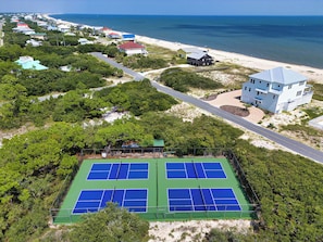 Luchtbeeld van een kustgebied met een tennisbaan, strand en woongebouwen.