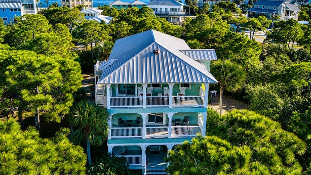 A multi-story house with a balcony, surrounded by lush greenery and a view of the ocean. - Top' Sea Turvy - Private Pool, 5 Minutes To Beach, Tennis & Pickleball Court! (St. George Island)