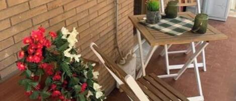 A patio area with a wooden bench, a small table, and a potted plant.