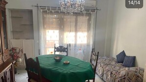 Un coin repas avec une table verte, des chaises, un lustre et un lit avec une literie à motifs.