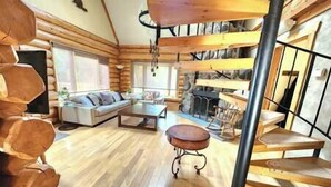 A log cabin interior with a living room, sofa, coffee table, and a fireplace.
