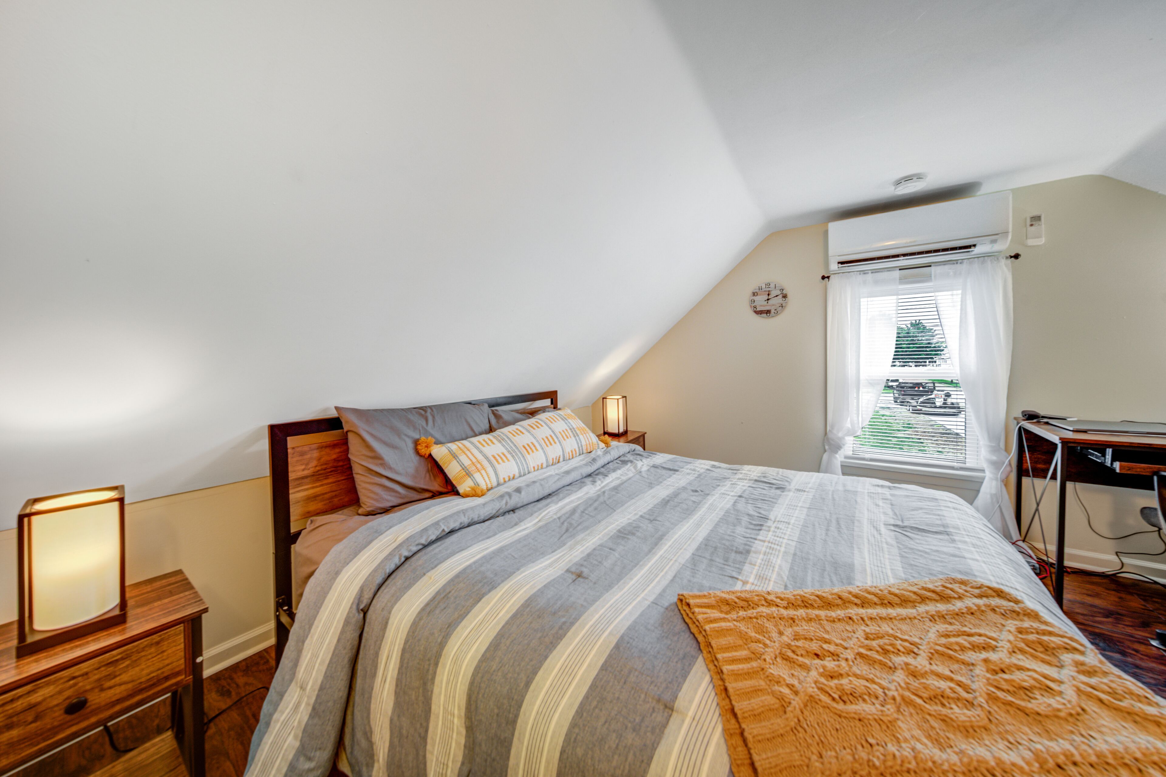 Ein Schlafzimmer mit Bett, Nachttischen, einer Lampe und einem Fenster mit Vorhängen.