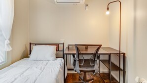 A small, well-lit room with a bed, a desk, a chair, and an air conditioning unit. - Cozy Chalet Bungalow in West Park - Cleveland (Cleveland)