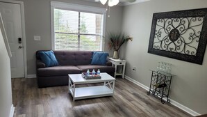 A living room with a brown sofa, white coffee table, and a decorative metal wall piece. - Chic, newly renovated townhome (North Charleston)