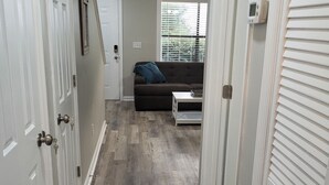 A hallway with a wooden floor, a dark brown sofa, and a white door with a keyhole. - Chic, newly renovated townhome (North Charleston)