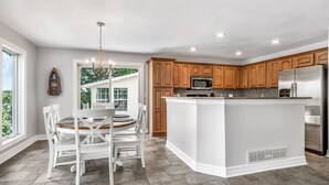 A modern kitchen with wooden cabinets, a central island, and a dining area with white chairs.