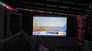 Un système de cinéma maison comprenant un grand écran, un espace détente et une guirlande de lumières colorées.