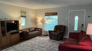 Un salon avec un canapé en cuir marron, un canapé rouge, un meuble de rangement en bois et un tapis à motifs.