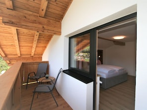 Un balcone con travi in legno, un tavolino con sedie e un letto nella stanza adiacente.