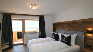 Ett sovrum med en dubbelsäng, en sänggavel i trä, utsikt över naturen genom ett fönster och ett litet bord med en stol.