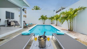 A pool area with a grill, lounge chairs, and a bottle of champagne. - NEW 5BR Villa w/ PrivatePool 3min to Eagle Beach (Noord)