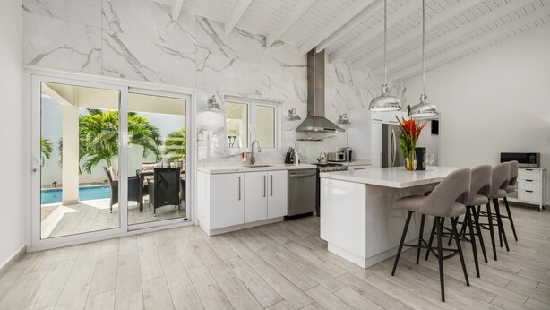 A modern kitchen with a large island, white cabinetry, and a view of a swimming pool. - NEW 5BR Villa w/ PrivatePool 3min to Eagle Beach (Noord)