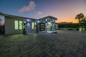 A modern house with a covered patio, potted plants, and a brick driveway.