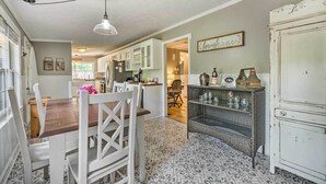 A spacious kitchen with white cabinetry, a dining area with a wooden table and white chairs, and a patterned floor. - Walk to Mount Dora Historic District: Cozy Home! (Mt Dora)
