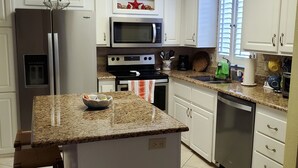 A kitchen with white cabinets, a granite countertop, a built-in microwave, a stainless steel refrigerator, and a dishwasher. - Cozy vacation home (Jensen Beach)