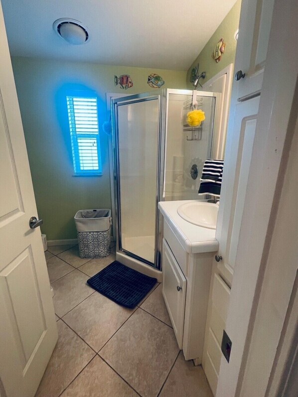 Un baño con ducha, inodoro, lavamanos y una ventana con persianas.