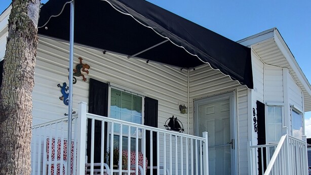 A white mobile home with a black awning, a porch with a white railing, and a staircase leading to the entrance. - Cozy vacation home (Jensen Beach)